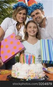 Portrait of a girl smiling with her parents holding birthday presents