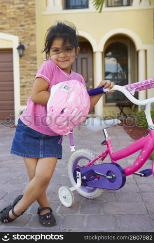 Portrait of a girl standing and holding a bicycle in front of a house