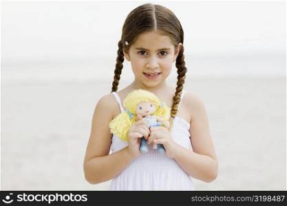 Portrait of a girl standing on the beach and holding a doll