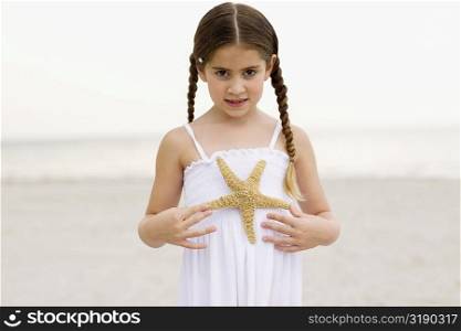 Portrait of a girl standing on the beach and holding a starfish