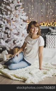 Portrait of a girl with a pretty face in the Christmas lights.. Beautiful girl sitting on the carpet near the Christmas tree 7204.