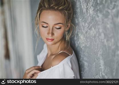 Portrait of a girl with an original hairstyle of blonde hair.. Close-up portrait of beautiful young girl near the gray wall 127.