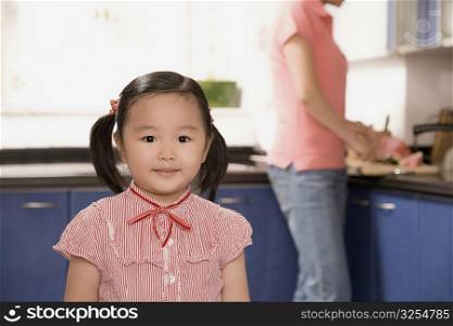 Portrait of a girl with her mother working in the background in the kitchen