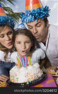 Portrait of a girl with her parents blowing candles on a birthday cake