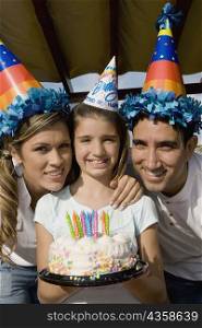 Portrait of a girl with her parents holding a birthday cake and smiling