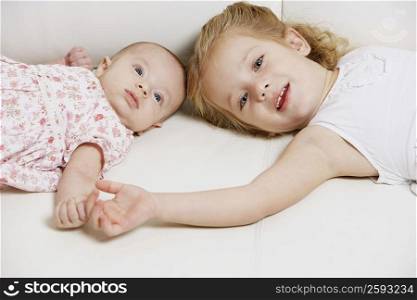 Portrait of a girl with her sister lying on the bed