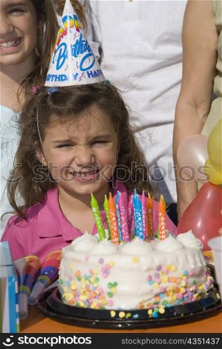 Portrait of a girl with her sisters standing in front of a birthday cake