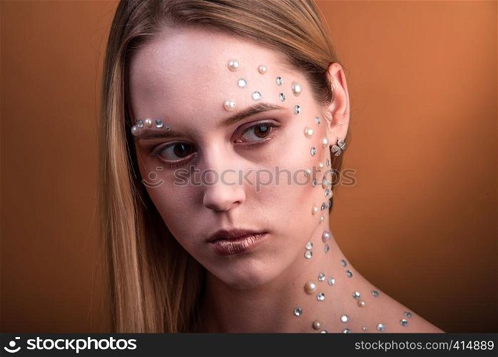 Portrait of a girl with original and creative makeup with white and pearl rhinestones. Girl with white and pearl rhinestones on her face.