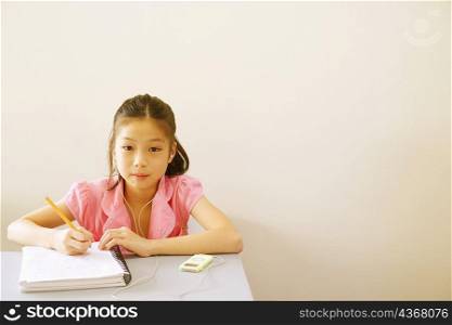 Portrait of a girl writing in a spiral notebook and listening to an MP3 player