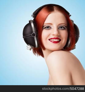 Portrait of a glamorous sexy girl, wearing big vintage music headphones and listening to the music on blue background.