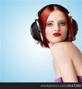 Portrait of a glamorous sexy girl, wearing big vintage music headphones and listening to the music on blue background.
