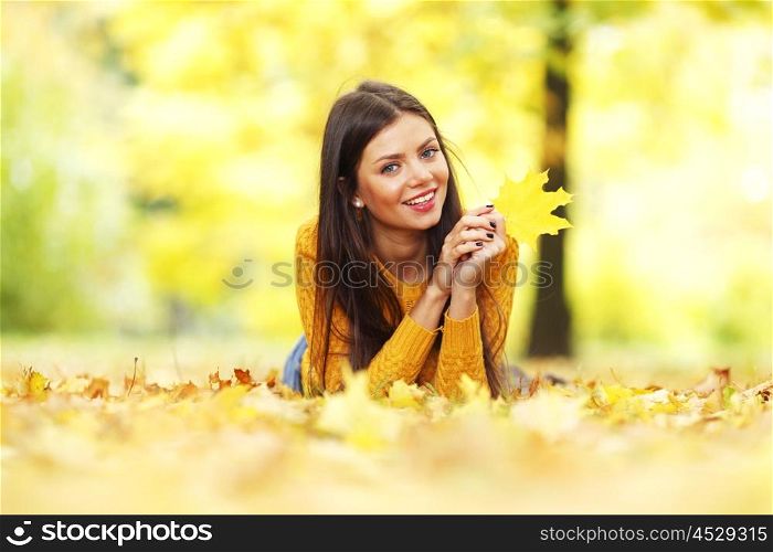 Portrait of a gorgeous brunette woman laying in the autumn park