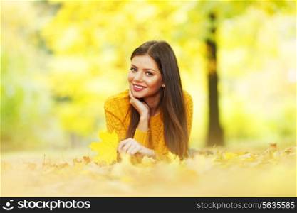 Portrait of a gorgeous brunette woman laying in the autumn park
