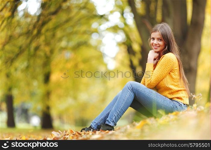 Portrait of a gorgeous brunette woman sitting in the autumn park. Woman in autumn park