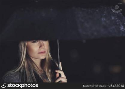 Portrait of a gorgeous sad woman standing under big black umbrella in rainy night, loneliness and sadness concept. Beautiful sad woman under the rain