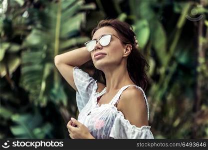 Portrait of a gorgeous woman in rainforest, attractive sexy model wearing stylish sunglasses, luxury photoshoot in the jungle, enjoying summer vacation on exotic island. Fashion woman portrait