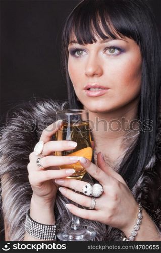 Portrait of a gorgeous young brunette with glass of sparkling wine on the black background. Woman with glass of sparkling wine