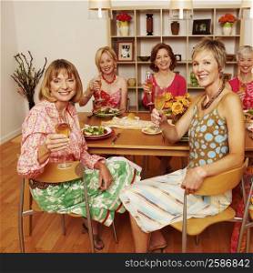 Portrait of a group of mature adult woman sitting at dining table holding champagne flutes