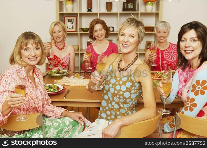 Portrait of a group of mature women sitting at the dining table and holding champagne flutes