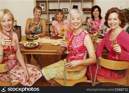 Portrait of a group of mature women sitting at the dining table and holding champagne flutes