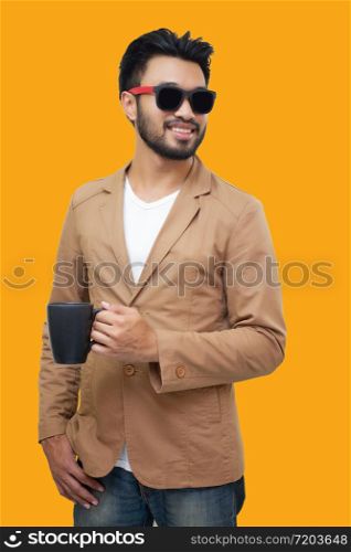 Portrait of a handsome asian young businessman holding an cup and drinking coffee. Isolated on yellow background.