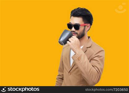 Portrait of a handsome asian young businessman holding an cup and drinking coffee. Isolated on yellow background.