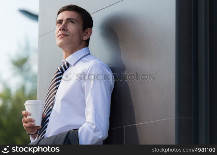 Portrait of a handsome businessman drinking coffee on the street near office building