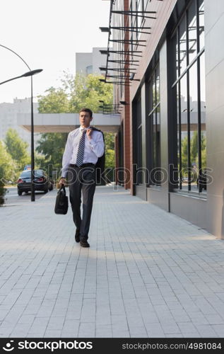 Portrait of a handsome businessman walking on the street near office building