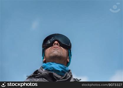 Portrait of a Handsome Man Dressing Ski Goggles Looking Up in the Sky over Blue Clear Sky Background. Active Lifestyle. Happy Vacation.. Man Skier Enjoying Winter Fresh Air