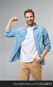 Portrait of a handsome man in jeans shirt showing his bicep with arm bended over grey background.. Portrait of a handsome man in jeans shirt showing his bicep with arm bended over grey background