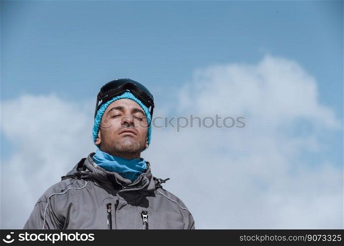 Portrait of a handsome man with closed eyes of pleasure enjoying bright sunny day in the mountains over blue sky background. Happy winter holidays.. Happy man in winter vacation