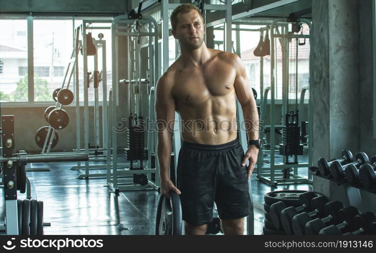 Portrait of a handsome muscular man is lifting dumbbells in fitness or gym. Healthy, Sport and Lifestyle Concept.