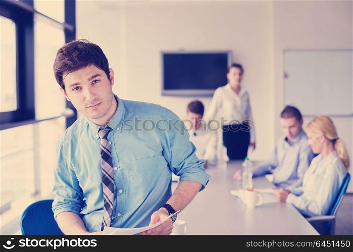 Portrait of a handsome young business man on a meeting in offce with colleagues in background