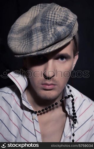 Portrait of a handsome young man with blue eyes, a gray cap on a black background