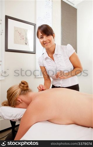 Portrait of a happy acupuncturist in her clinic with a female patient
