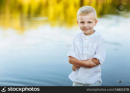 Portrait of a happy and beautiful little boy with blond hair and a white shirt, Happy childhood. Positive emotion. portrait near the river in nature.. Portrait of a happy and beautiful little boy with blond hair and a white shirt, Happy childhood. Positive emotion. portrait near the river in nature