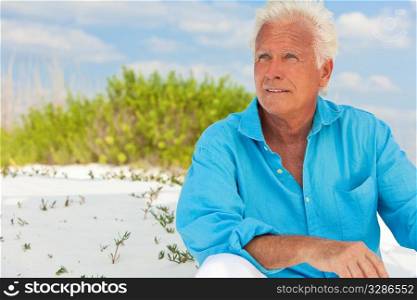 Portrait of a happy attractive handsome senior man sitting down outside on a white sand beach