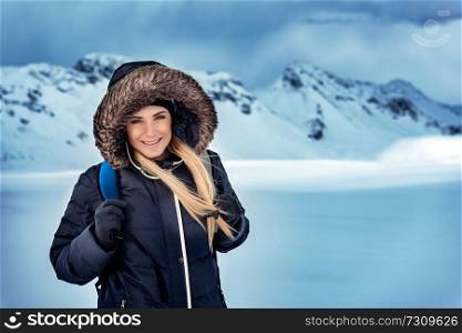 Portrait of a happy beautiful woman with backpack traveling in the snowy mountains, trekking in the North Pole, active winter holidays