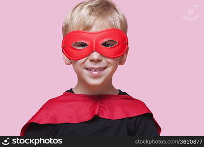 Portrait of a happy boy in superhero costume over pink background