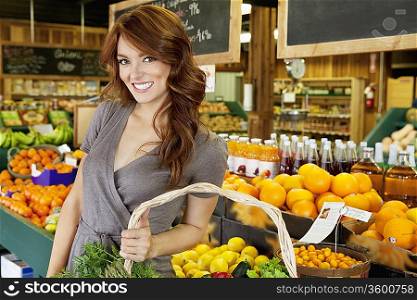 Portrait of a happy brunette woman standing with basket in fruit market