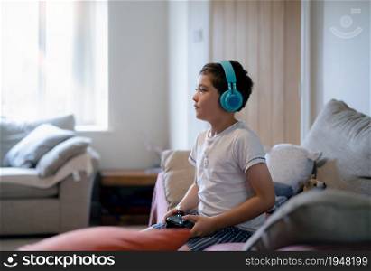 Portrait of a happy child wearing headphones and looking up with smiling face,Happy young boy listening to music, Cute Kid sitting on sofa playing video game or relaxing in living room at home