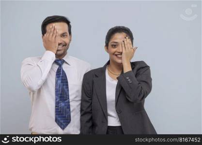 Portrait of a happy corporate couple covering one eye with palms and looking at camera through one eye