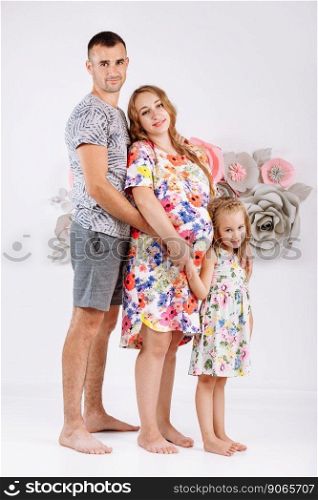 Portrait of a happy family father, pregnant mother, little daughter having fun together isolated over white with floral background.. Portrait of a happy family father, pregnant mother, little daughter having fun together isolated over white with floral background