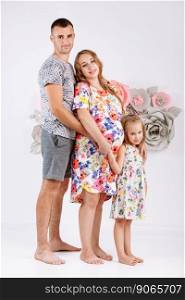 Portrait of a happy family father, pregnant mother, little daughter having fun together isolated over white with floral background.. Portrait of a happy family father, pregnant mother, little daughter having fun together isolated over white with floral background