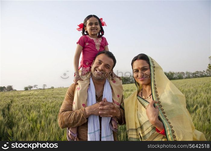 Portrait of a happy family in field with girl on father&rsquo;s shoulders