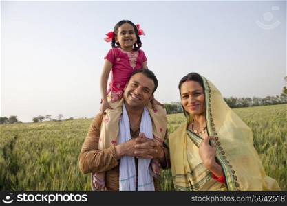 Portrait of a happy family in field with girl on father&rsquo;s shoulders