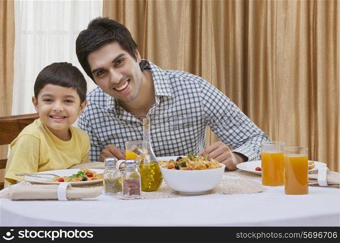 Portrait of a happy father and son having pizza at table