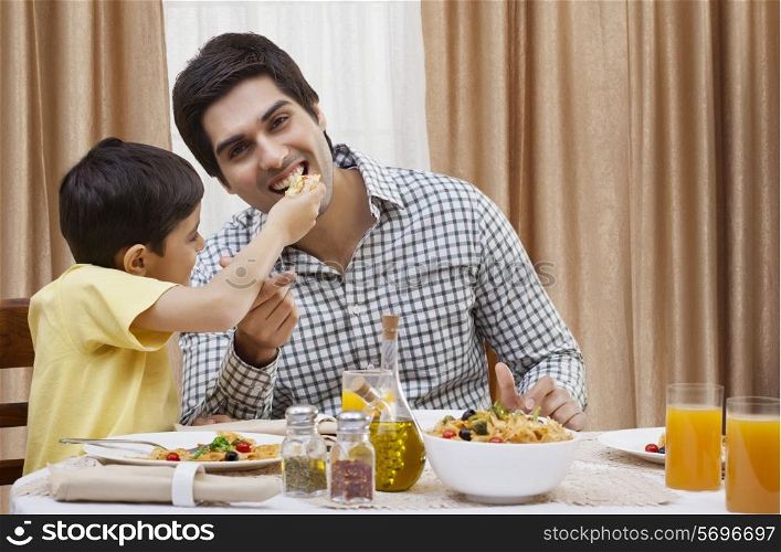 Portrait of a happy father being fed a piece of pizza by his son