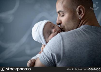 Portrait of a happy father with gentleness kissing his newborn baby, young family with pleasure spending time at home, love concept