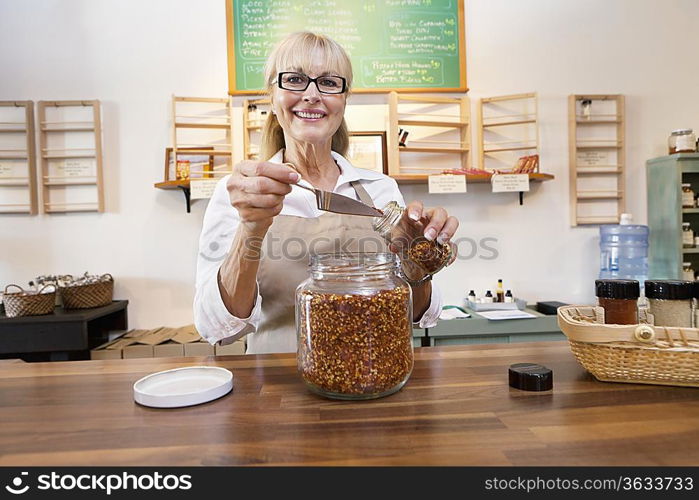 Portrait of a happy female employee pouring spice with scoop in jar